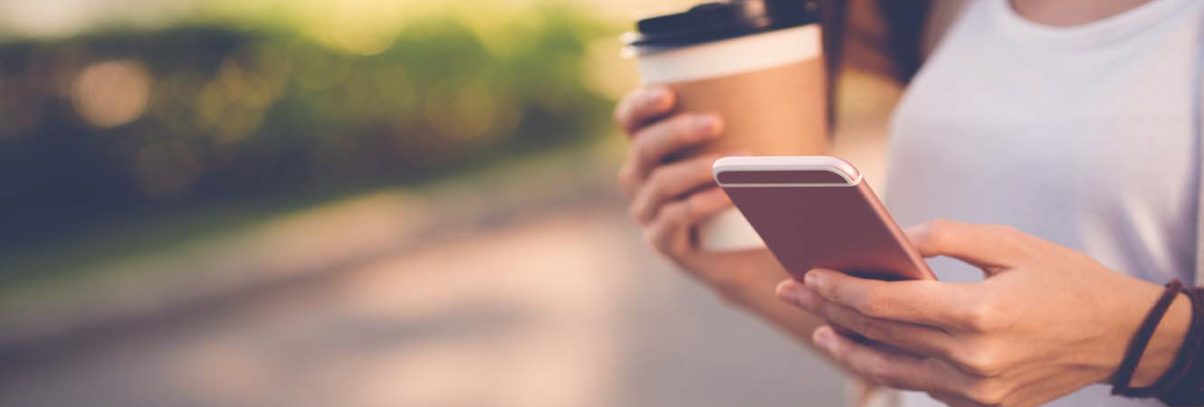A girl checking her phone as she holds coffeee in other hand
