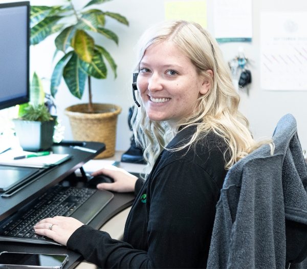 A customer service representative is sitting at her desk and looking over her shoulder, smiling.