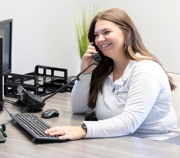 A female employee sits at her desk as she talks on the phone and types on her computer.