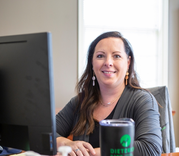 A female mortgage lender sits at her desk smiling with her arms folded.