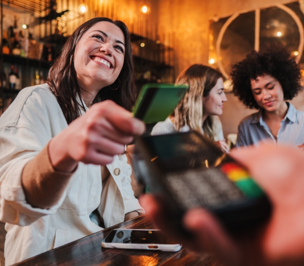 A smiling woman pays her tab at a bar using her debit card.