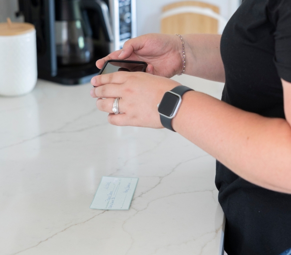 A person holding a mobile phone takes a photo of a check using the mobile check deposit feature on their banking app.