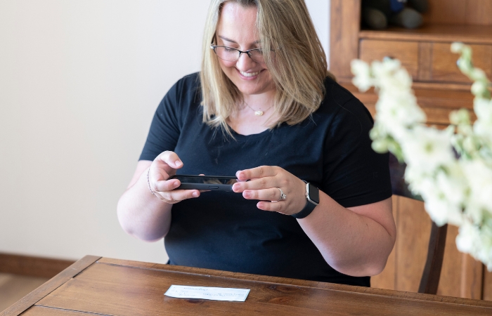 A young woman sits at a table while using mobile deposit on her smart phone.