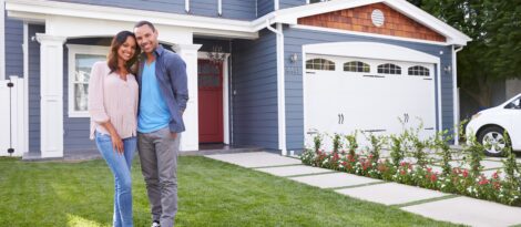 A couple stands in front of their blue family home.