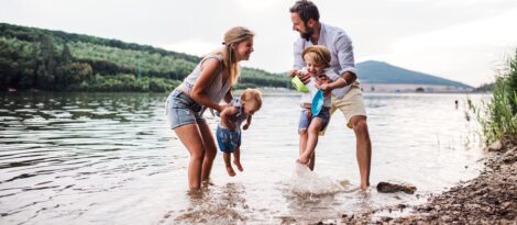 A couple and their two children stand in a river and play in the water and sand.