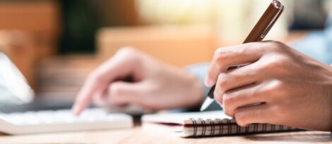 A close up of hands working on a calculator and holding a pen over a checkbook.