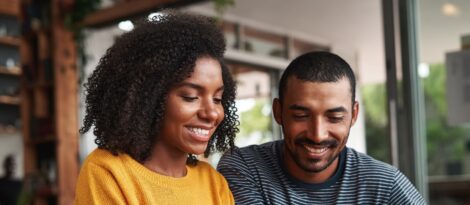 A Black woman and Black man site next to each other and look at something below them and off screen.