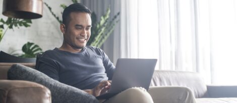 A man sits on a couch and browses on his laptop.