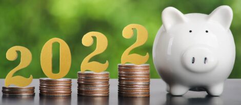 The numbers 2022 sitting on stacks of coins next to a piggy bank.