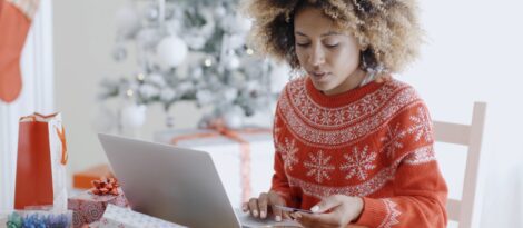 A woman in a winter sweater shops online using her laptop computer.