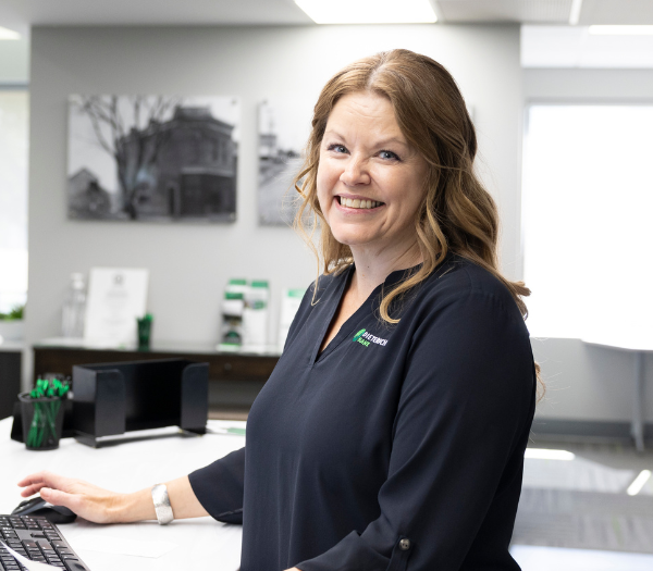 A retail banker smiling at the viewer from the side of the teller line.