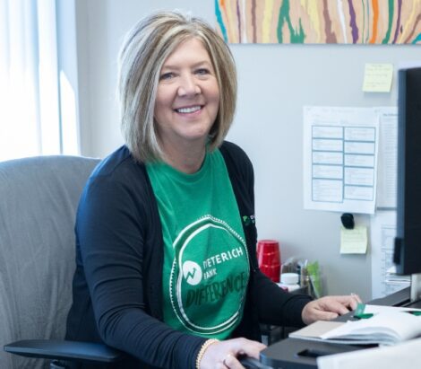 A woman smiles at the camera while sitting at her desk.